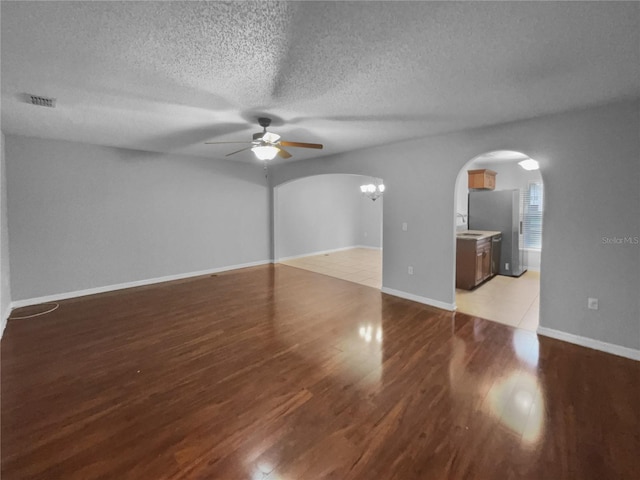 empty room featuring arched walkways, visible vents, light wood-style floors, a textured ceiling, and baseboards