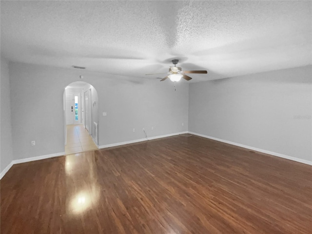 empty room with arched walkways, ceiling fan, a textured ceiling, wood finished floors, and baseboards