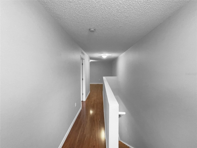 hallway featuring a textured ceiling, dark wood finished floors, an upstairs landing, and baseboards