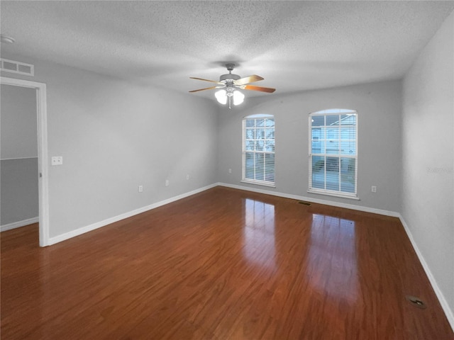 empty room featuring a textured ceiling, wood finished floors, visible vents, baseboards, and a ceiling fan