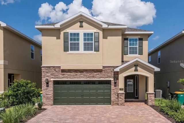 view of front of property with central AC, stucco siding, decorative driveway, stone siding, and an attached garage