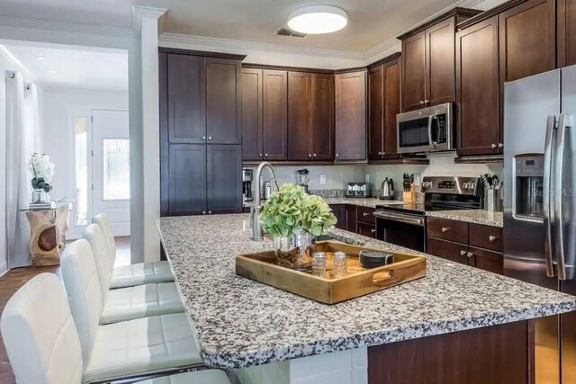 7568 Marker Ave, Kissimmee, FL 34747 - kitchen featuring visible vents, a breakfast bar, ornamental molding, appliances with stainless steel finishes, and dark brown cabinets