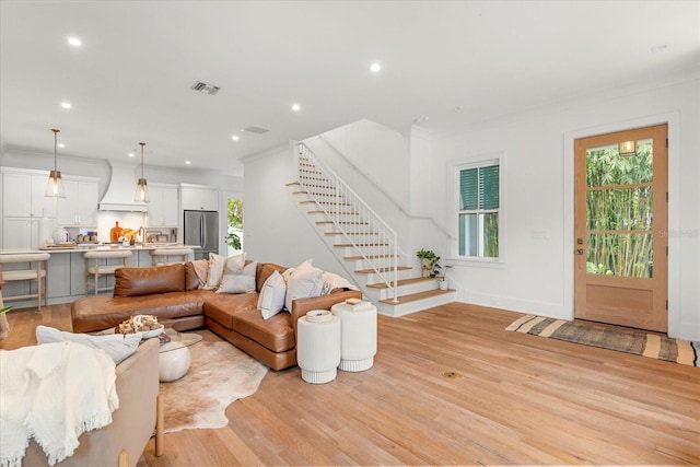 living room with light wood-type flooring, visible vents, plenty of natural light, and stairs