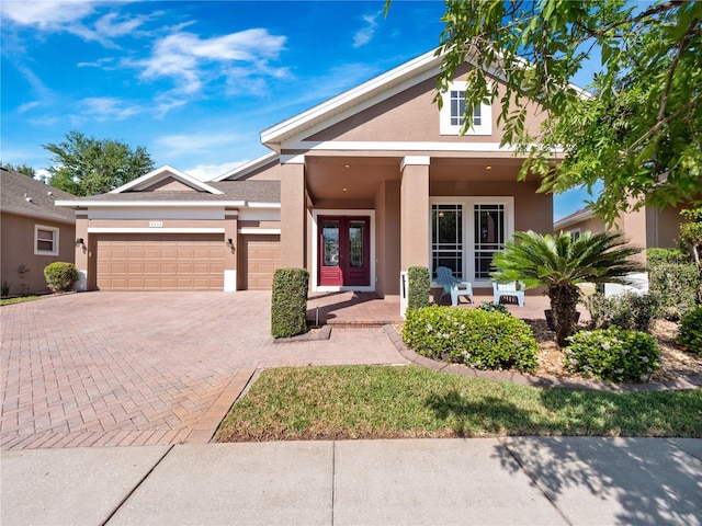 view of front of property featuring stucco siding, decorative driveway, french doors, covered porch, and a garage