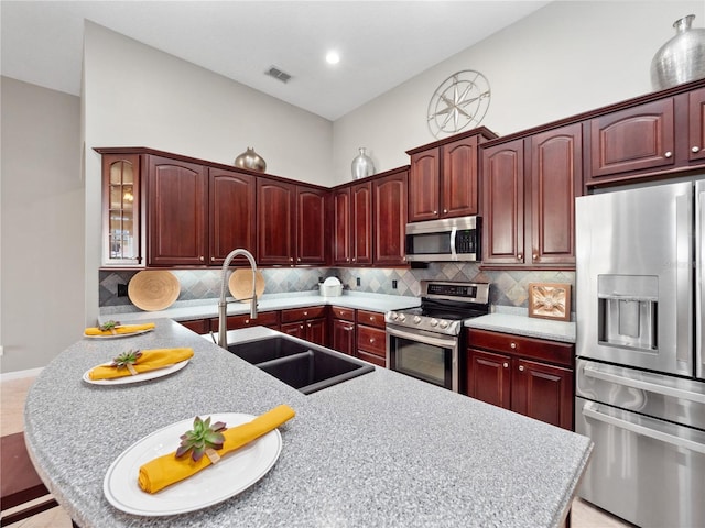 kitchen with reddish brown cabinets, stainless steel appliances, light countertops, and a sink