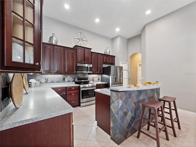 kitchen featuring a breakfast bar area, arched walkways, light countertops, appliances with stainless steel finishes, and backsplash