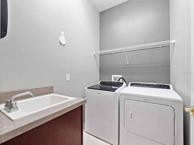 washroom featuring a sink, a textured ceiling, washing machine and dryer, light tile patterned floors, and laundry area