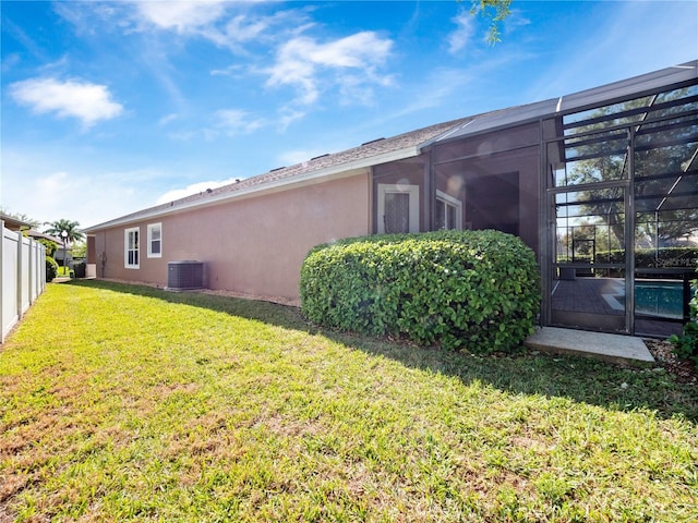 back of house featuring fence, central AC, a lawn, glass enclosure, and stucco siding