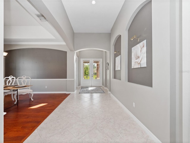 tiled entrance foyer with arched walkways, visible vents, french doors, and baseboards