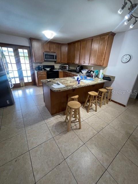 kitchen with light tile patterned floors, stainless steel microwave, black range with electric stovetop, a peninsula, and stone counters