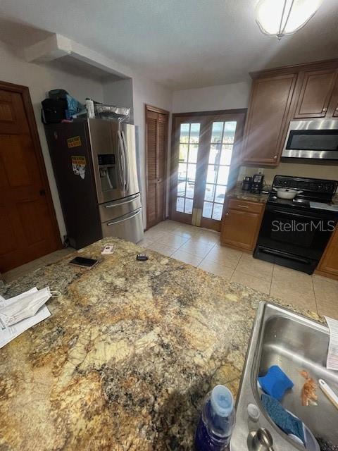 kitchen with stone countertops, appliances with stainless steel finishes, a sink, and light tile patterned flooring