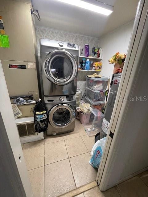 clothes washing area featuring electric water heater, stacked washer and dryer, tile patterned flooring, and laundry area