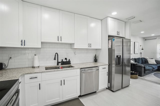 kitchen featuring open floor plan, appliances with stainless steel finishes, a sink, and white cabinets