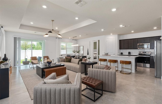 living area featuring light tile patterned floors, a tray ceiling, visible vents, and recessed lighting