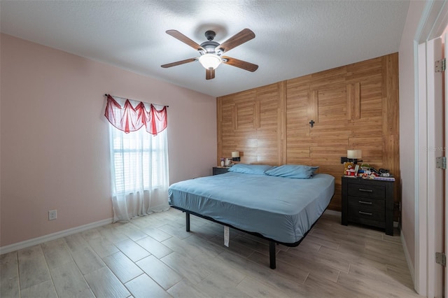 bedroom with a textured ceiling, light wood-type flooring, a ceiling fan, and baseboards