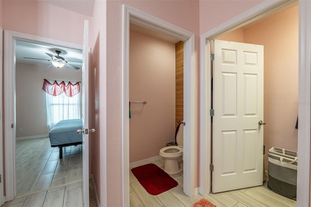 ensuite bathroom with toilet, wood tiled floor, baseboards, and a ceiling fan