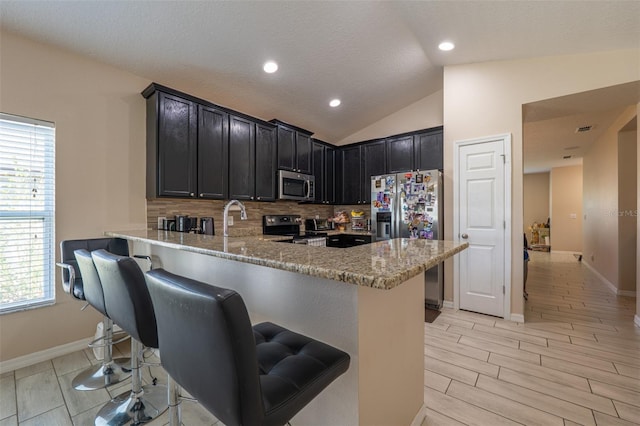 kitchen with stainless steel appliances, lofted ceiling, light stone countertops, a peninsula, and a kitchen bar