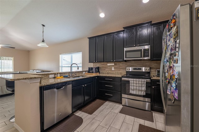 kitchen with light stone counters, a peninsula, a sink, appliances with stainless steel finishes, and tasteful backsplash