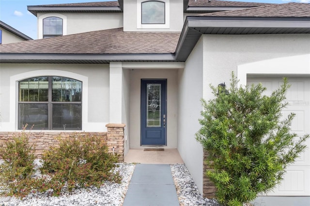 view of exterior entry featuring stone siding, stucco siding, an attached garage, and a shingled roof