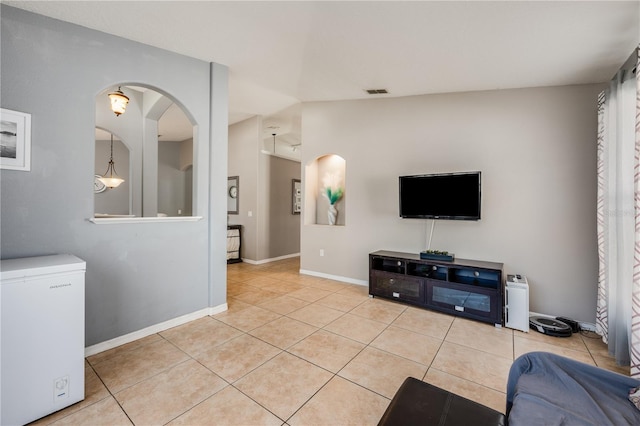 tiled living room featuring lofted ceiling, visible vents, and baseboards