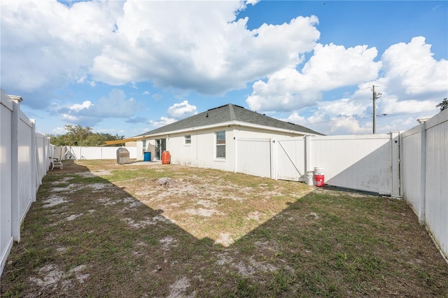 back of house featuring a fenced backyard, a gate, and a yard