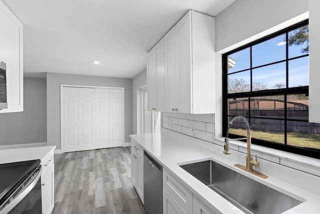 kitchen with light countertops, appliances with stainless steel finishes, white cabinetry, a sink, and light wood-type flooring