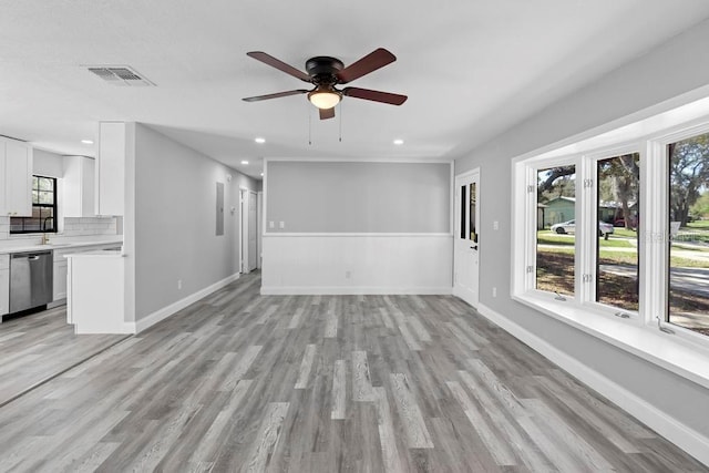 unfurnished living room featuring light wood finished floors, a sink, visible vents, and baseboards