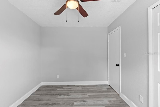 spare room featuring a textured ceiling, wood finished floors, a ceiling fan, and baseboards