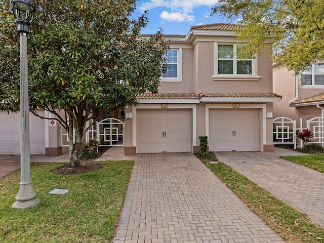 townhome / multi-family property with driveway, a tile roof, a garage, and stucco siding