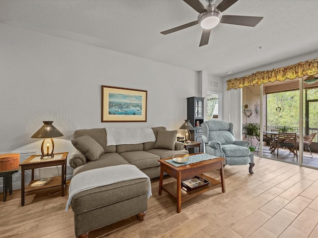 living room featuring light wood-style floors, a ceiling fan, visible vents, and a textured ceiling