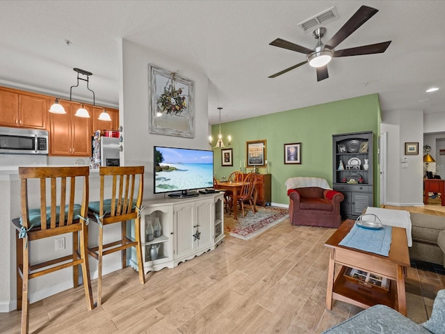 living area with ceiling fan with notable chandelier, baseboards, visible vents, and light wood-style floors