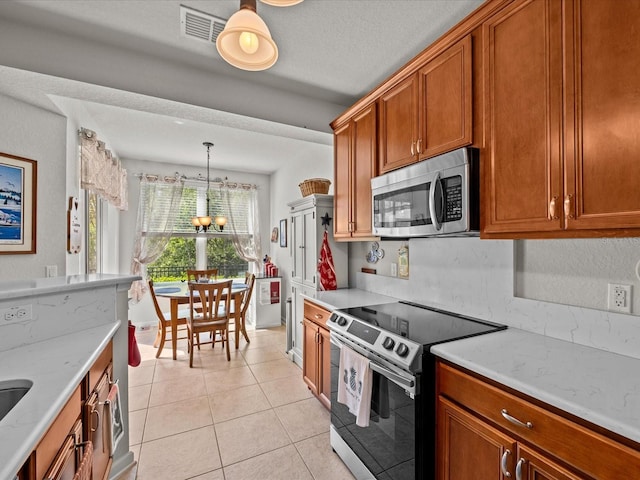 kitchen with brown cabinetry, light stone countertops, stainless steel appliances, a notable chandelier, and light tile patterned flooring