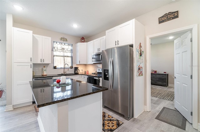 kitchen featuring white cabinets, decorative backsplash, a kitchen island, stainless steel appliances, and a sink