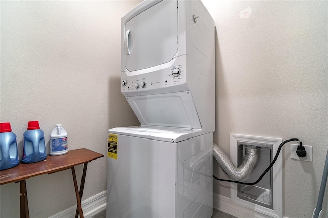 laundry area featuring baseboards, laundry area, a textured wall, and stacked washer / drying machine