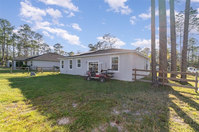 rear view of house featuring a yard, fence, and stucco siding