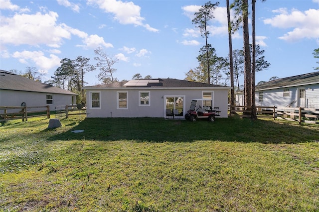 back of house featuring a lawn, stucco siding, fence, and roof mounted solar panels