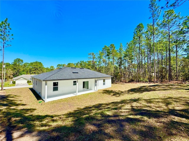 back of house featuring a yard, a shingled roof, and stucco siding