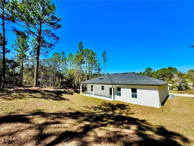 rear view of property with a patio area, stucco siding, a yard, and roof with shingles