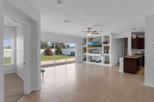 unfurnished living room featuring a textured ceiling, ceiling fan, built in shelves, and baseboards