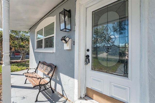 entrance to property featuring stucco siding, covered porch, and fence