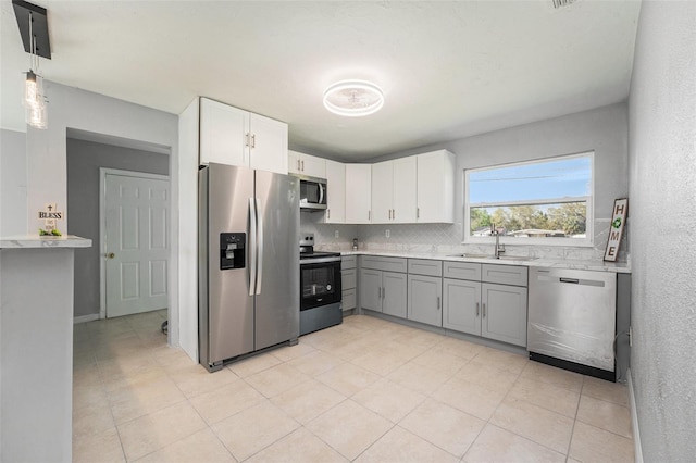 kitchen with gray cabinetry, a sink, backsplash, stainless steel appliances, and light countertops