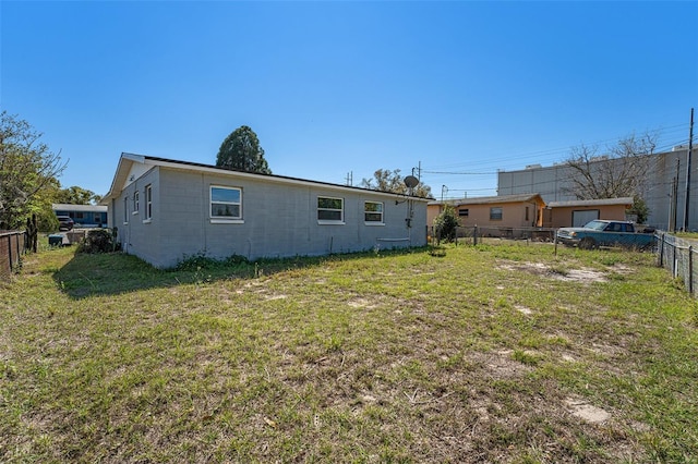 rear view of house featuring concrete block siding, fence private yard, and a lawn