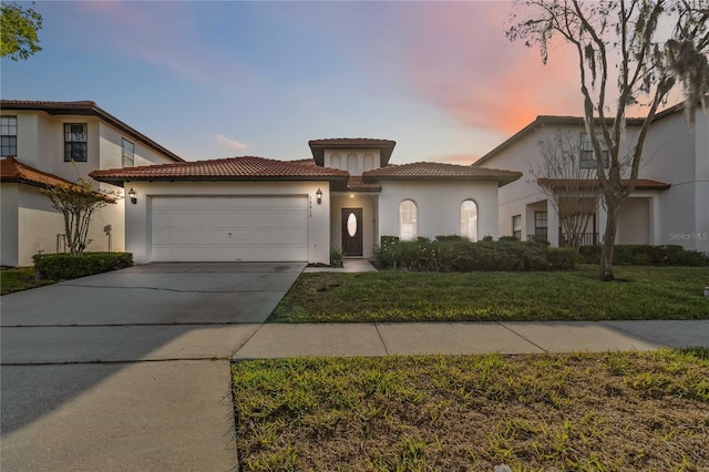 mediterranean / spanish-style house with a front lawn, a tile roof, concrete driveway, stucco siding, and an attached garage