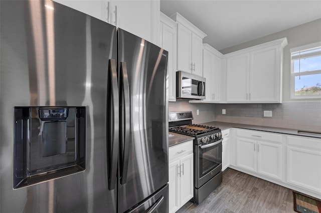 kitchen with dark countertops, wood finished floors, white cabinetry, appliances with stainless steel finishes, and decorative backsplash