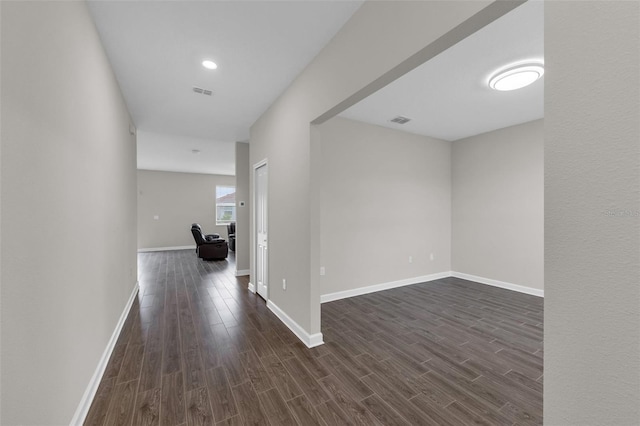 corridor featuring visible vents, baseboards, and dark wood-style floors