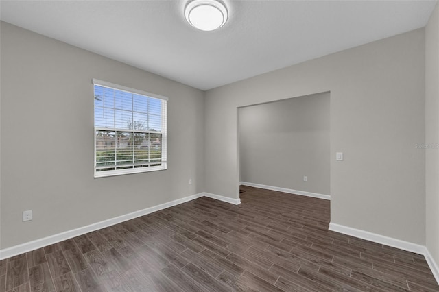 spare room with baseboards and dark wood-style flooring