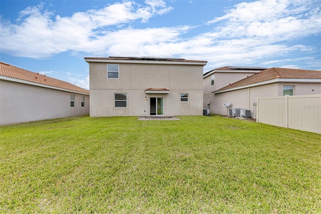 back of property featuring stucco siding, a lawn, solar panels, fence, and central AC unit