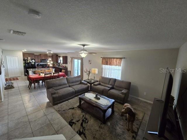 living room featuring light tile patterned floors, visible vents, baseboards, ceiling fan, and a textured ceiling