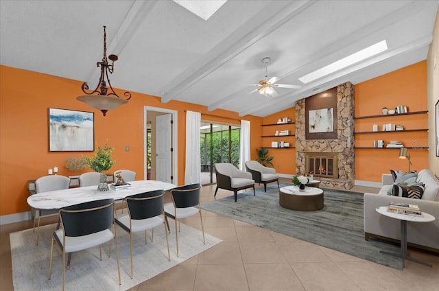 dining room featuring baseboards, light tile patterned floors, a stone fireplace, vaulted ceiling with skylight, and a ceiling fan