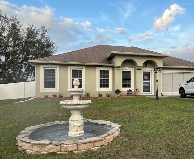 ranch-style house featuring a shingled roof, an attached garage, fence, a front lawn, and stucco siding